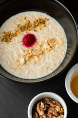 Semolina porridge for breakfast oat with nuts in black bowl served with honey isolated on black stone background. Homemade food. Tasty breakfast.