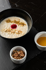 Semolina porridge for breakfast oat with nuts in black bowl served with honey isolated on black stone background. Homemade food. Tasty breakfast.