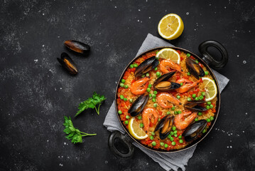 Traditional Spanish paella with seafood in a frying pan on a black stone background. Top view, flat lay. Mediterranean Kitchen.