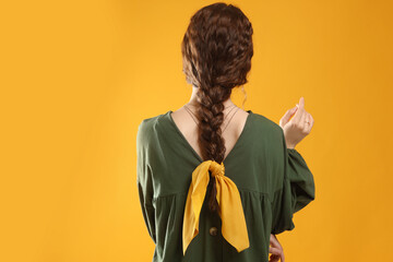 Woman with stylish bandana on yellow background, back view