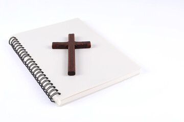 Wooden christian cross placed on a book with white background with writing area