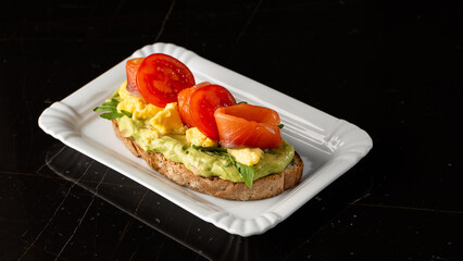 Buckwheat bread toast with an egg, a sliced avocado, a salmon, tomatoes and lettuce. Dietary menu. Flat lay.