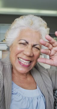 Vertical shot of a senior biracial woman having a video call, blowing a kiss to the camera