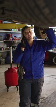 Vertical shot of a female mechanic talking on the phone under a suspended car