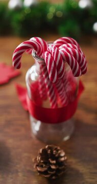 Vertical close-up shot of candy canes in a jar surrounded by Christmas decorations on a wooden table