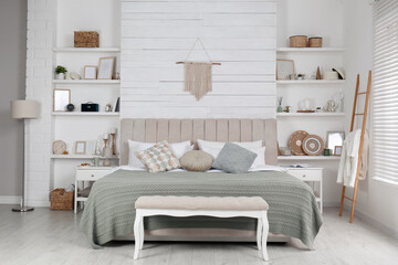 Stylish room interior with large comfortable bed, wall shelves and beautiful decor elements