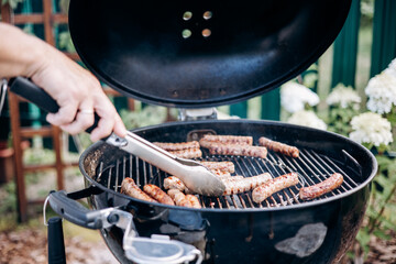 Backyard BBQ. Close-up of grilling sausages of meat on barbecue. Man preparing tasty sausages