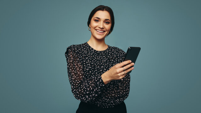 Carefree young woman holding a smartphone in a studio