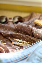Brown polka dot blouse, vintage mom jeans, straw bag, round sunglasses, gold rings and pearl hair clips. Fashionable outfit on wooden background. Selective focus.
