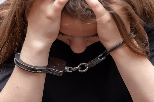A young girl handcuffed on a gray background, close-up. Juvenile delinquent in a black T-shirt, criminal liability of minors.