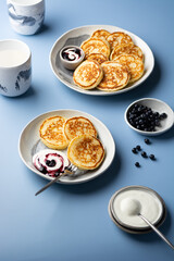 Cottage cheesecakes with sour cream and blueberry jam in a plate served on a blue background with cups of milk. Traditional Russian syrniki on breakfast.