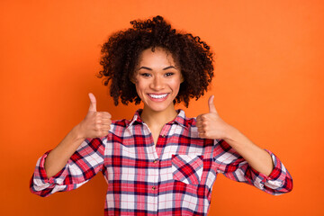 Photo of cute young brunette lady thumb up wear plaid shirt isolated on orange color background