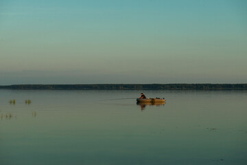 The boat floats on the calm blue water of the lake. fishermen set sail early in the morning for fishing. silence and grace, photos in blue tones, a panarama of a lake view. copy space.