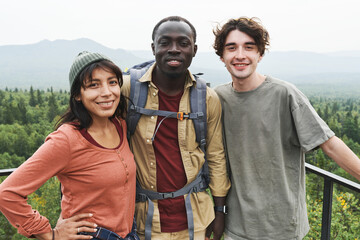 Portrait of positive young multi-ethnic friends standing on bridge against beautiful forest landscape