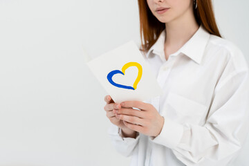 Cropped view of blurred woman holding card with blue and yellow heart sign isolated on white.