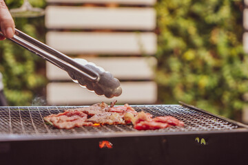 Close up view of pieces of sliced beef on charcoal grill at Outdoor party. Human's hands using meat tongs to grill Multiple slices of premium meat on the stovetop. Home made barbecue beef grill smoke.