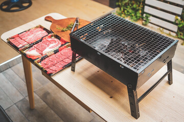 Close up of charcoal grill with raw sliced beef set on wooden table at Outdoor party. Home made barbecue beef grill smoke.