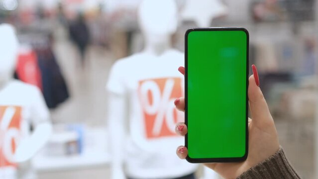 Big sale. Lots of discount coupons to save money on your smartphone. A girl is holding a phone with a green screen in a shopping center. black Friday.
