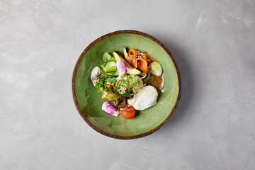 Salad bowl with salmon, avocado, broccoli, vegetables and egg on homemade ceramic plate. Buddha bowl with salmon, broccoli, quinoa in modern serveware. Modern ceramic dishware on concrete background.