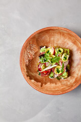 Salad with pastrami, vegetables and dressing on handmade ceramic bowl. Vegetables salad with roast beef in modern dishware on gray stone background. Contemporary food from chef. Handmade dinner plate.