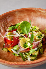 Salad with pastrami, vegetables and dressing on handmade ceramic bowl. Vegetables salad with roast beef in modern dishware on gray stone background. Contemporary food from chef. Handmade dinner plate.
