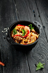 Japanese stir fryed udon noodles in wok. Udon noodle with chiken and vegetables on wooden background. Asian noodles on black table with ingredients. Wok menu.