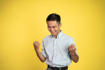 excited asian young man with two hands clenched on isolated background