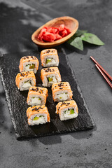 Maki sushi on dark slate. Hot philadelphia maki with baked salmon. Sushi roll with grilled salmon, cream cheese and avocado. Style concept japanese menu with black background, leaves and hard shadow.