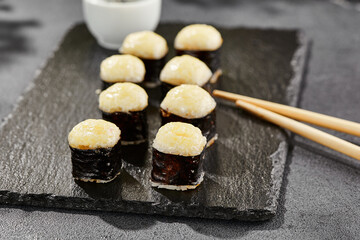 Baked Maki sushi on dark slate. Hot cheese hosomaki roll. Simple sushi roll with cheese, baked cheese topped. Style concept japanese menu with black background, leaves and hard shadow.