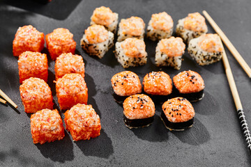 Hot maki set on dark slate. Baked sushi set with hot rolls. Sushi rolls with salmon,tobiko and baked cheese topped. Style concept sushi menu with black background, leaves and hard shadow.