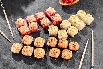 Hot maki set on dark slate. Baked sushi set with variety rolls. Sushi rolls with salmon,tobiko, crab and baked cheese topped. Style concept sushi menu with black background, leaves and hard shadow.