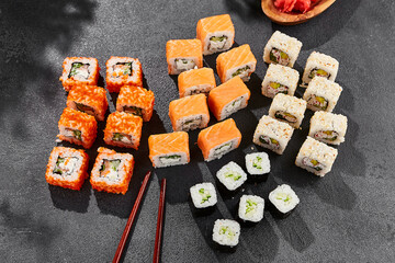 Maki sushi set on dark slate. Maki set with variety rolls. Composition from sushi rolls - philadelphia, california, hosomaki . Style concept sushi menu with black background, leaves and hard shadow.