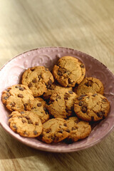 Pink plate filled with chocolate chip cookies on wooden table. Selective focus.