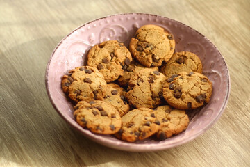 Pink plate filled with chocolate chip cookies on wooden table. Selective focus.