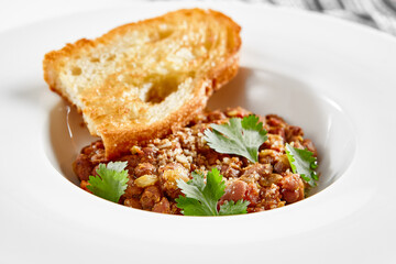 Georgian lobio in white plate with bread. Traditional georgian dish from red bean in sauce and spices.  Vegetarian appetizer from georgian cuisine. Caucasus lobio in restaurant menu. Vegan food.