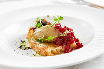 Chicken liver pate on crispy bread with red currant jam and micro green. Bruschetta with chicken pate in white plate. Delicious appetizer - foie gras on toast. Liver pate with jam in rustic style.