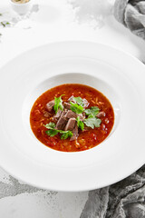 Authentic georgian beef soup Kharcho. Georgian lamb and rice soup. Caucasian dish - kharcho soup with rice, beef and coriander leaves. Kharcho in white plate on stone table.