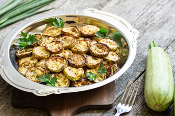 Fried zucchini with parsley in plate on rustic background, vegetarian food