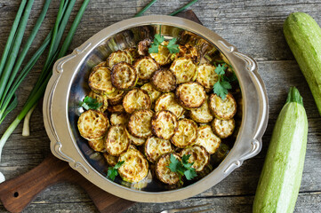 Fried zucchini with parsley in plate on rustic background, vegetarian food