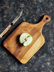 Slice of green apple on wooden cutting board and knife on black concrete background. Granny smith....