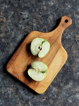 Slice of green apple on wooden cutting board on black concrete background with copy space. Granny smith. Spring fruits background.