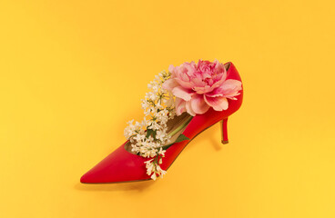 Minimal concept with blooming white lilac and pink peony in a shoe. Creative idea on yellow...
