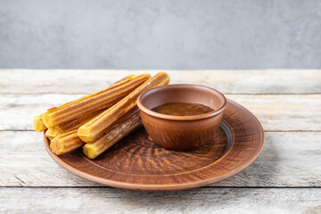 Churros on a plate and chocolate sauce on a wooden background
