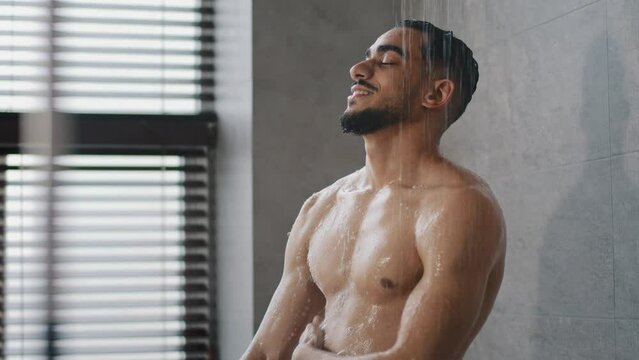Muscular Arabian sexy naked male Indian model sportsman guy 30s handsome relaxing bare wet man washing in bathroom with liquid soap shower gel foam water casual refreshment wash skincare body care