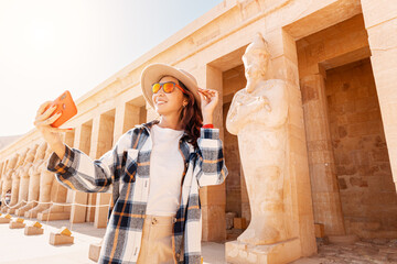 Travel blogger girl takes selfie pictures on a smartphone at the famous Hatshepsut temple in the...