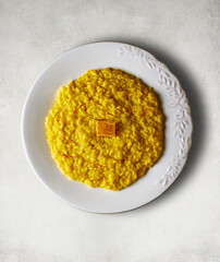 Risotto alla Milanese dressed with saffron threads and a Parmigiano Reggiano cheese rind on a white stone table. Italian cuisine.
