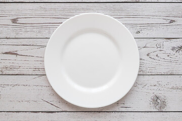 Plate on the background of a wooden tabletop. View from above. Small flat round white plate. Place for text.