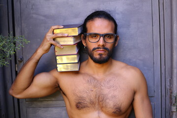 Shirtless man holding a pile of books 