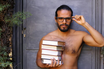 Shirtless man holding a pile of books 