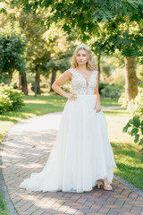 Obraz premium Wedding. Young beautiful bride with hairstyle and makeup posing in white dress and veil. Soft sunset light summer portrait. Girl looking in camera